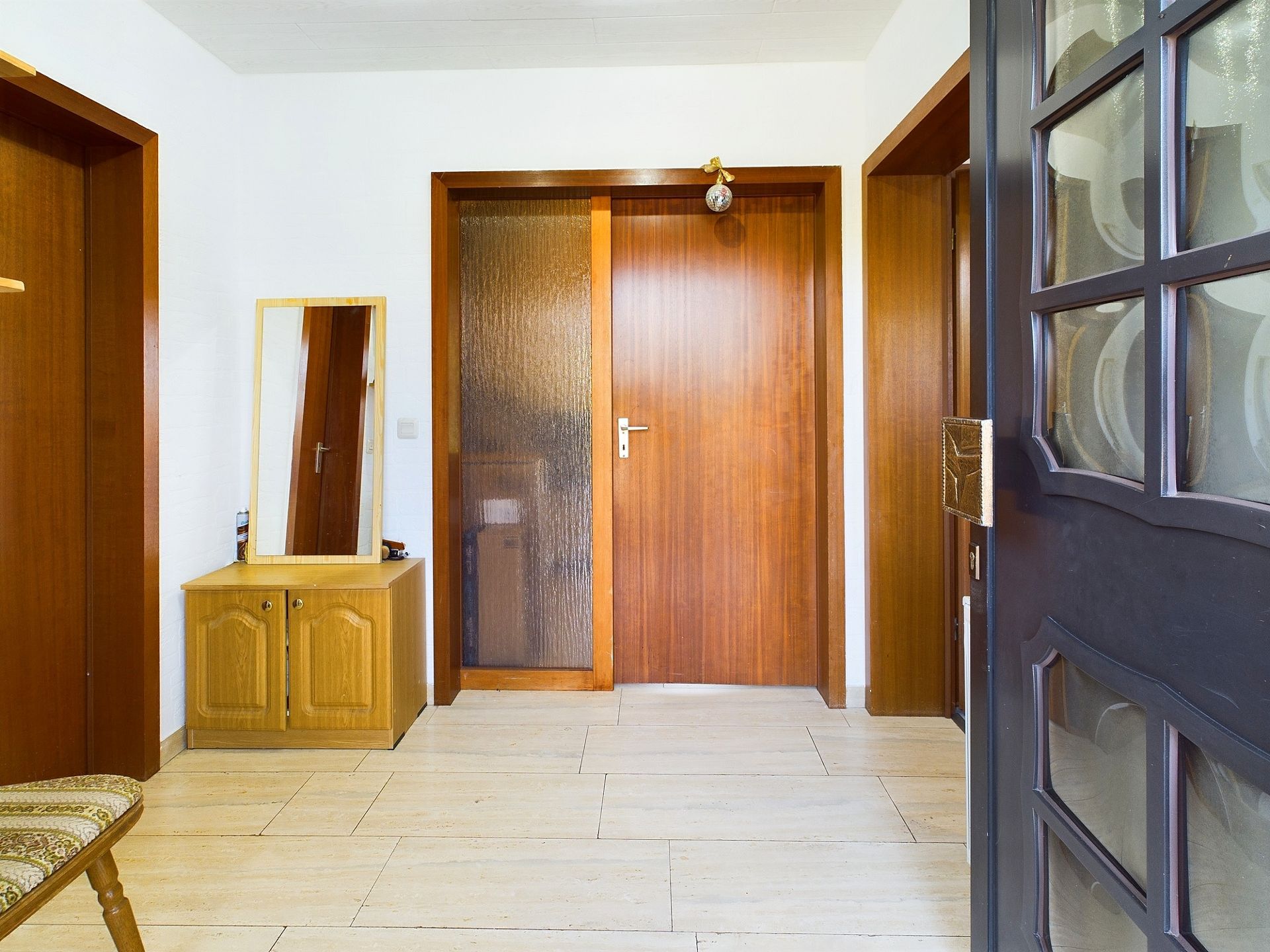 Heller Flur mit Holztüren, Spiegel auf Holzschrank und Fliesenboden.