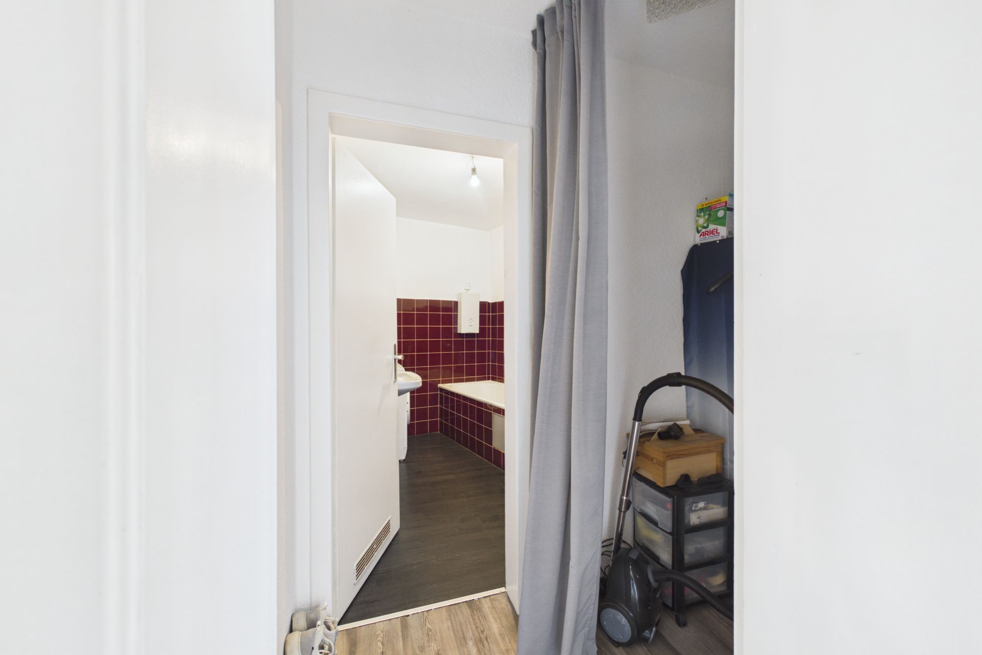 Blick durch geöffnete Tür in ein Bad mit roten Fliesen und weißer Badewanne.