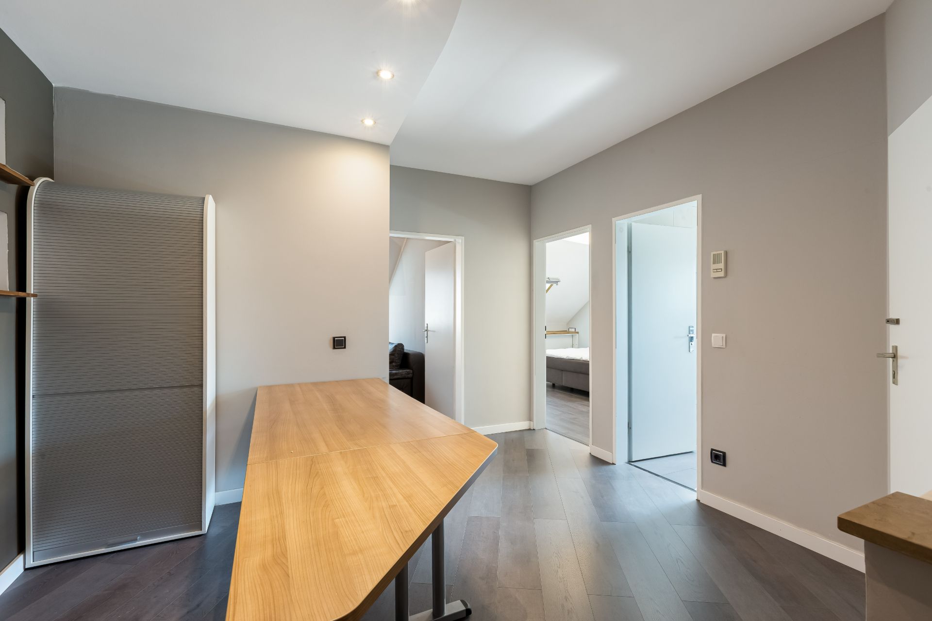 Moderner Flur mit Holztisch, grauem Schrank und zwei offenen Türen zu anderen Räumen.