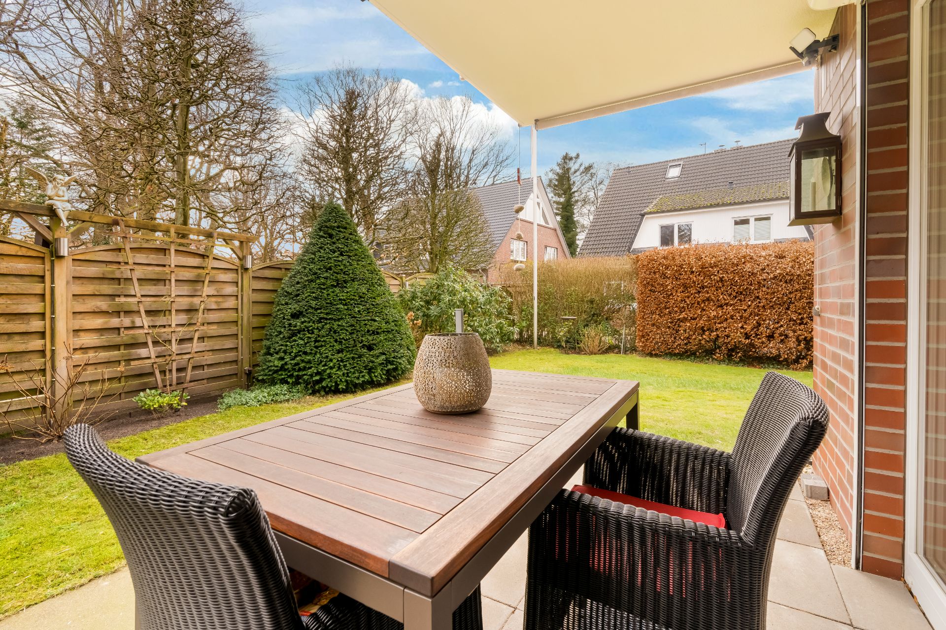 Terrasse mit Holztisch, zwei Stühlen, Garten und Blick auf Nachbarhäuser.