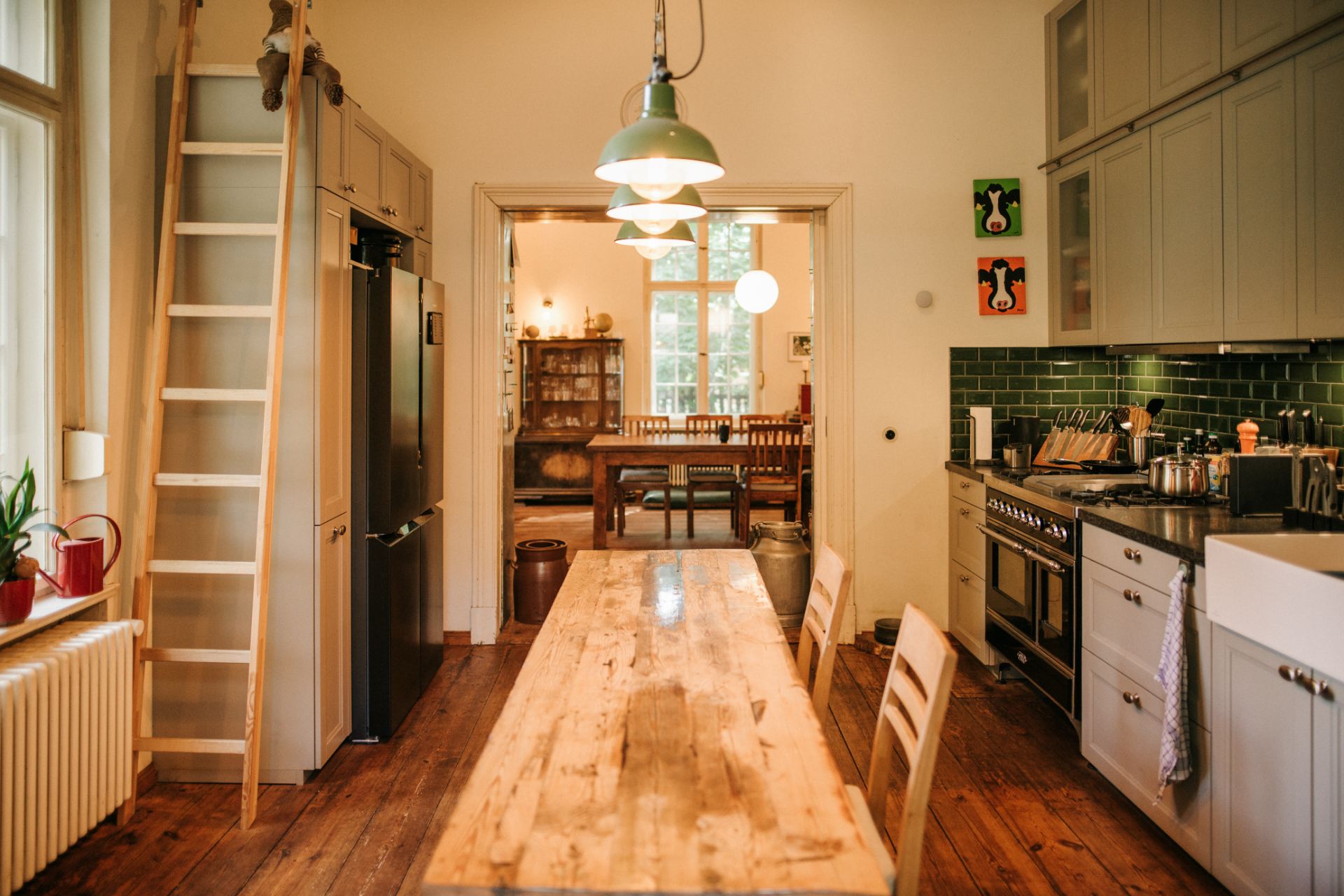 Helle Küche mit Holztisch, Leiter, großen Fenstern und Blick ins Esszimmer.