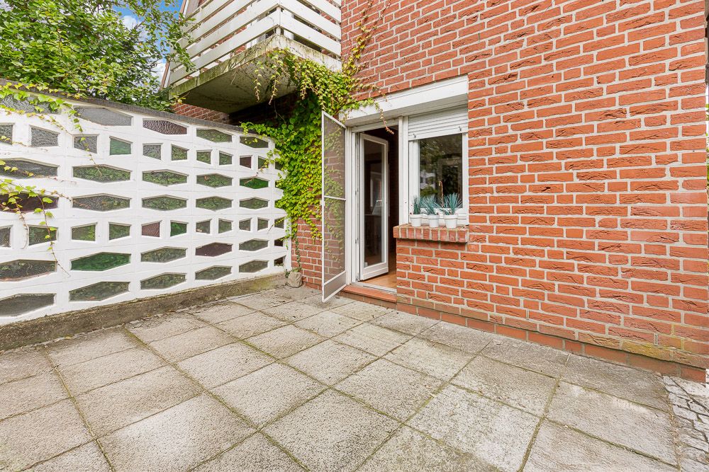 Gepflasterte Terrasse mit geöffneter Tür, roter Backsteinwand und weißer Sichtschutzmauer.