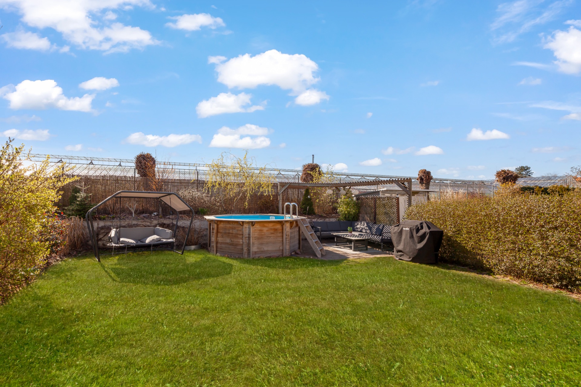 Garten mit Pool, Hollywoodschaukel, Sitzbereich und Rasen unter blauem Himmel.
