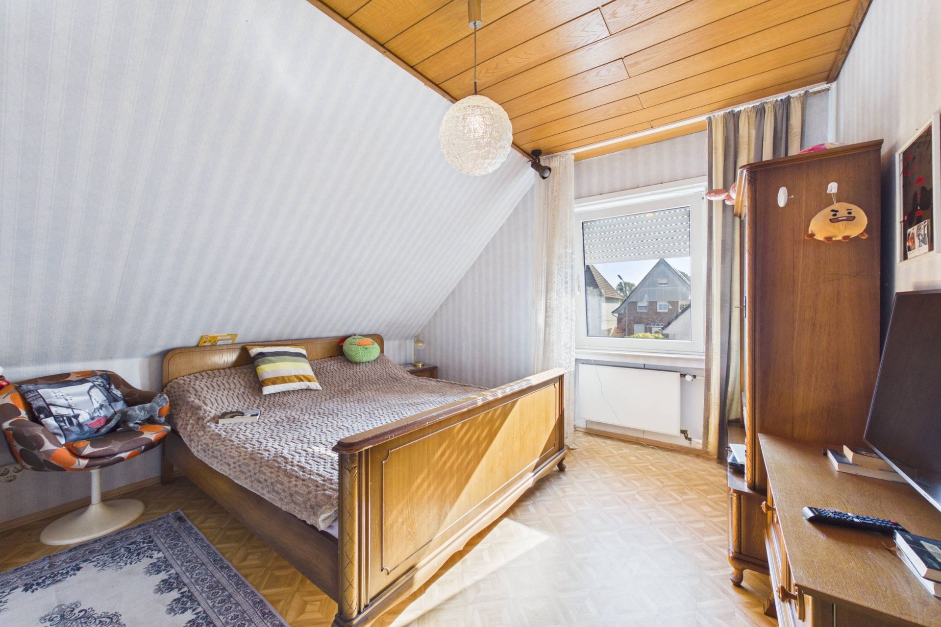 Helles Schlafzimmer mit Holzbett, Schreibtisch, Stuhl und Fenster unter einer Dachschräge.