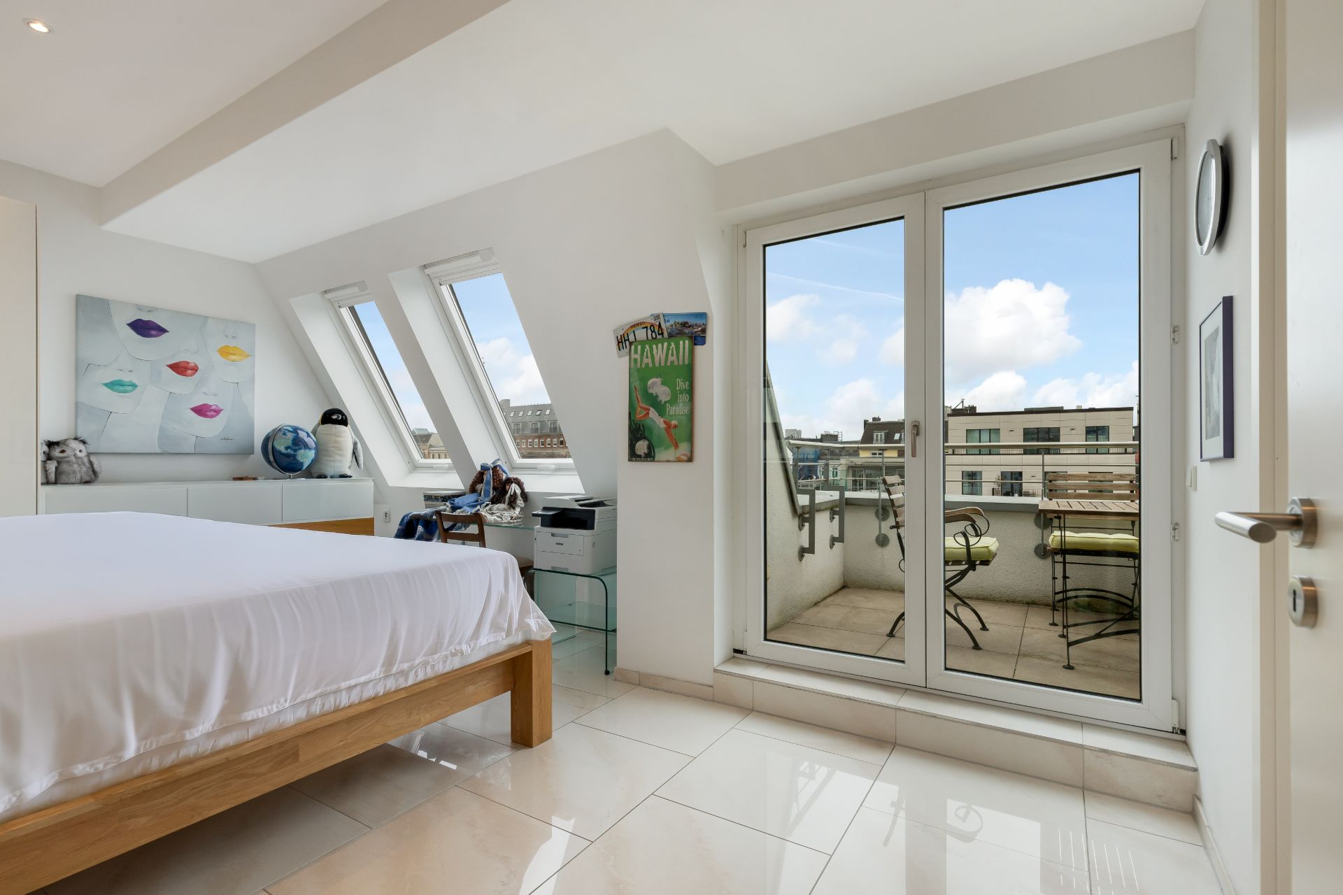 Helles Schlafzimmer mit Doppelbett, Schreibtisch und Zugang zu Balkon mit Sitzmöbeln.