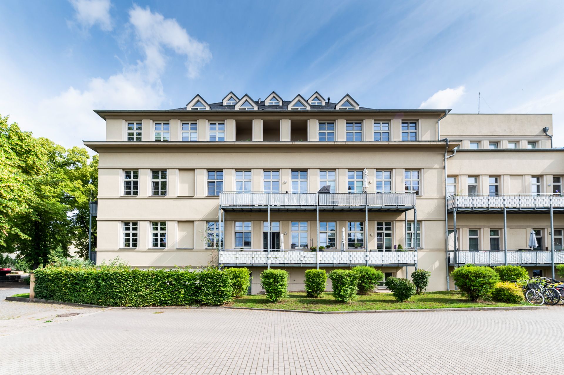 Dreistöckiges Wohngebäude mit Balkon und gepflegtem Vorgarten an einem sonnigen Tag.