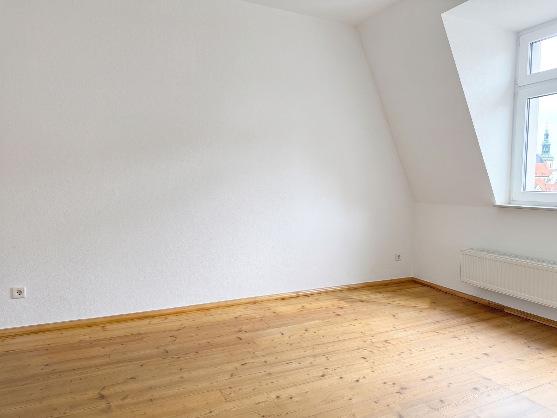Leerer Raum mit weißer Wand, Holzfußboden und Fenster mit Heizkörper.