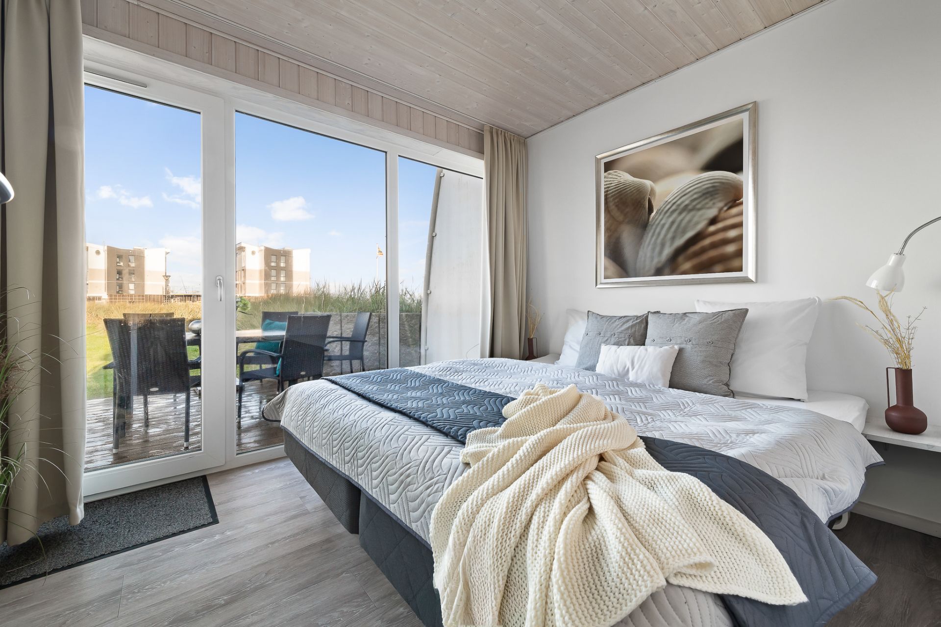 Modernes Schlafzimmer mit großem Bett, Glasfront und Zugang zu einer Terrasse mit Sitzgruppe.