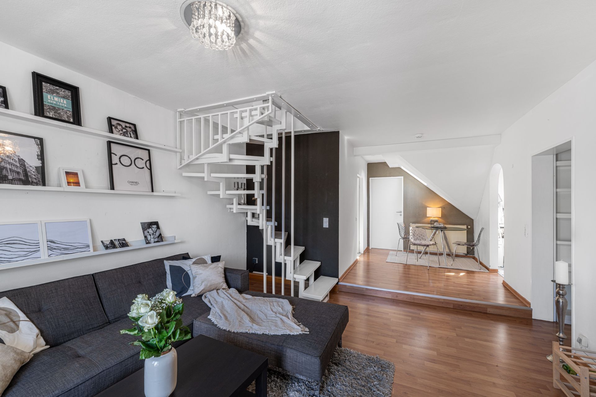 Modernes Wohnzimmer mit grauem Sofa, Treppe und kleinem Essbereich unter Dachschräge.