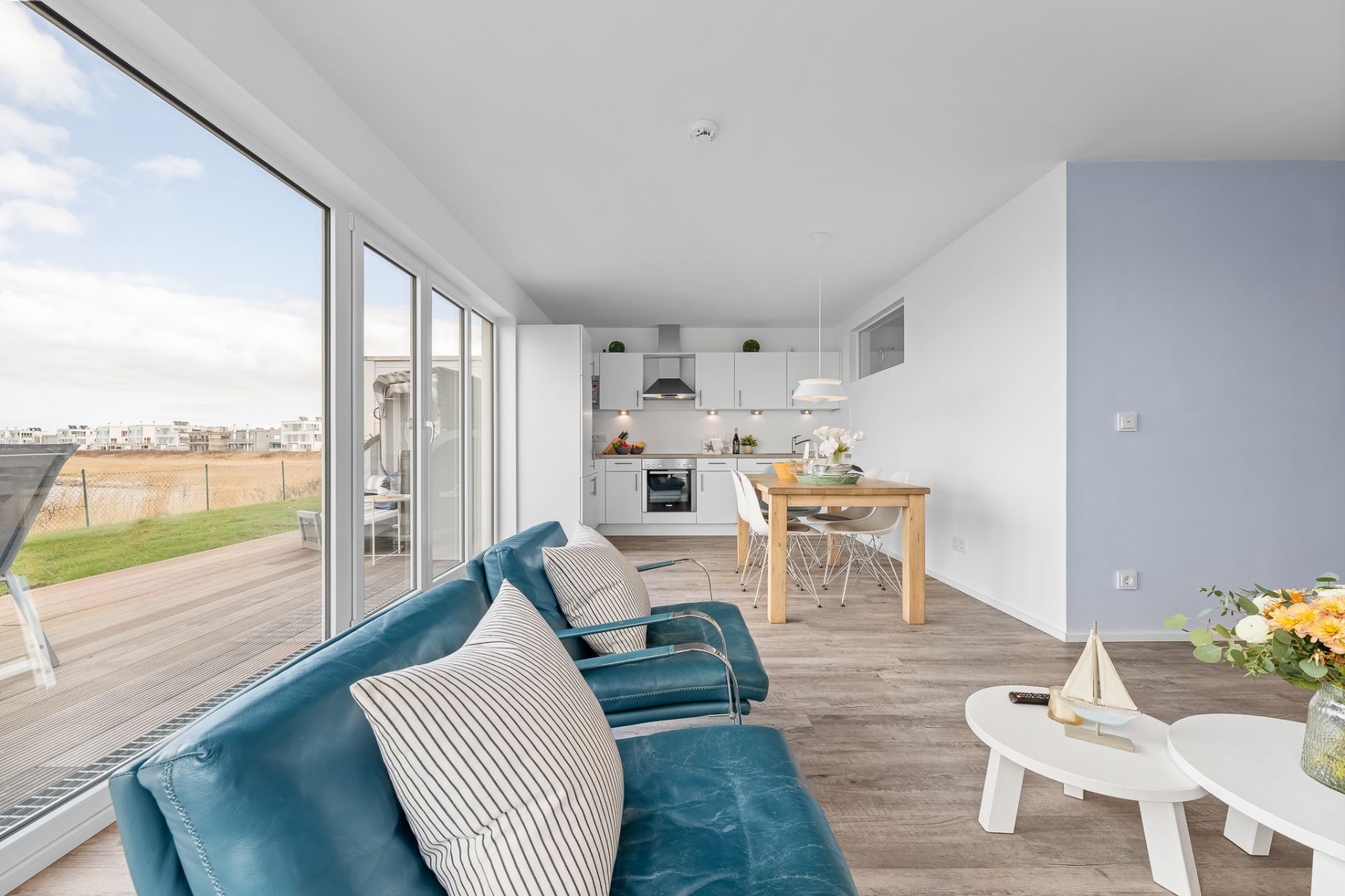 Helles Wohnzimmer mit blauer Couch, Essbereich, offener Küche und Zugang zur Terrasse.