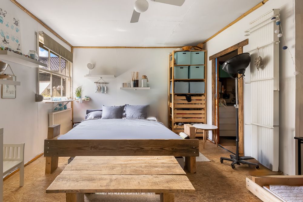 Gemütliches Schlafzimmer mit Holzbett, Regalen, großen Fenstern und Deckenventilator.