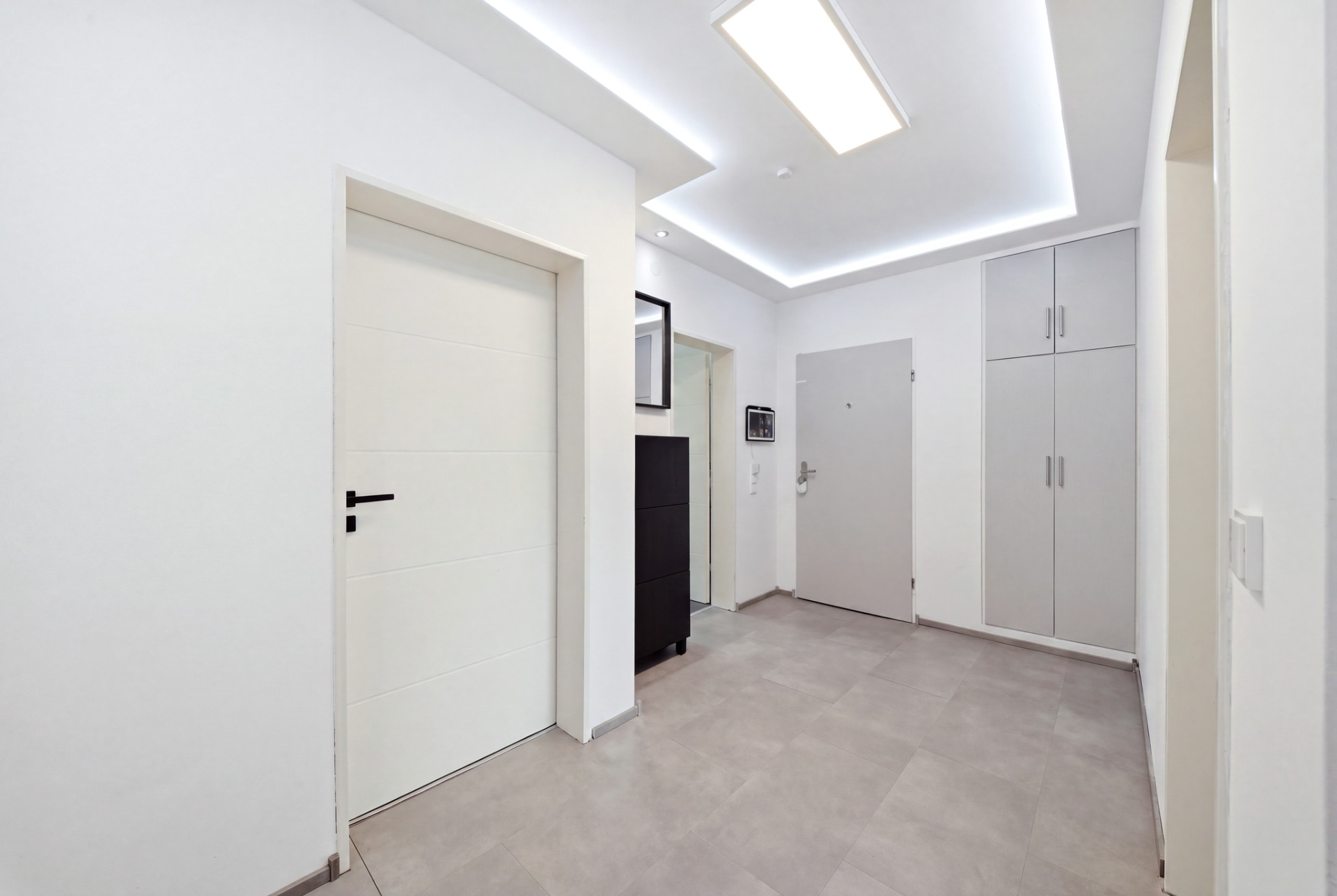 Heller Flur mit weißen Wänden, grauer Tür, Einbauschrank und Deckenbeleuchtung.
