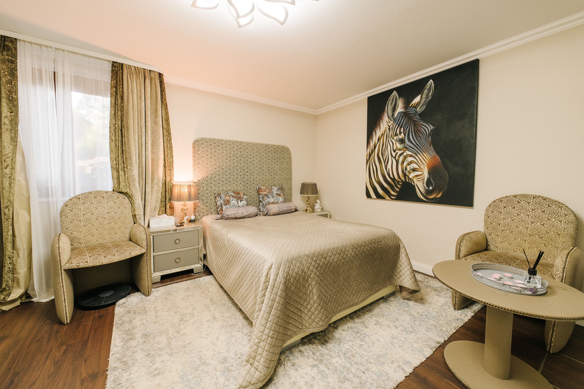 Schlafzimmer mit Doppelbett, zwei Sesseln, Teppich und einem großen Zebrabild an der Wand.