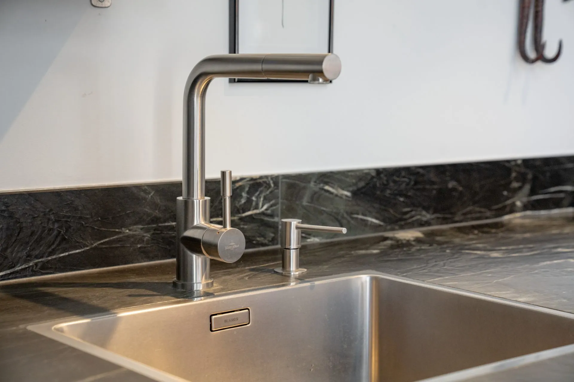 Moderne Edelstahlspüle mit Wasserhahn und Seifenspender auf dunkler Arbeitsplatte.