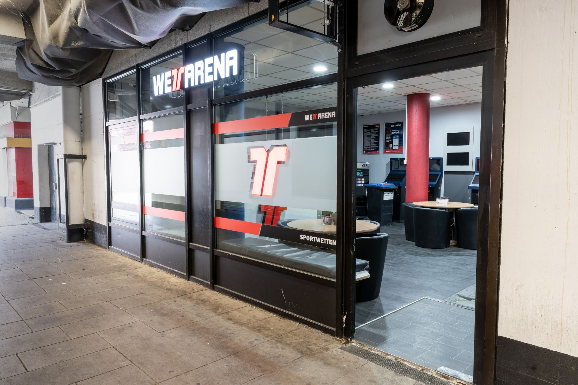 Eingang zu einem Wettbüro mit Sitzbereichen und Automaten im Inneren.