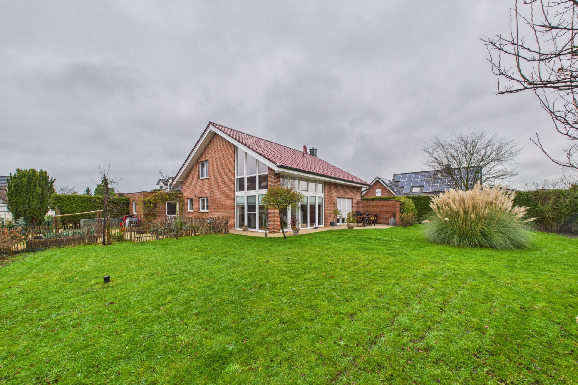 Modernes Einfamilienhaus mit großem Garten und vielen Fenstern an einem bewölkten Tag.
