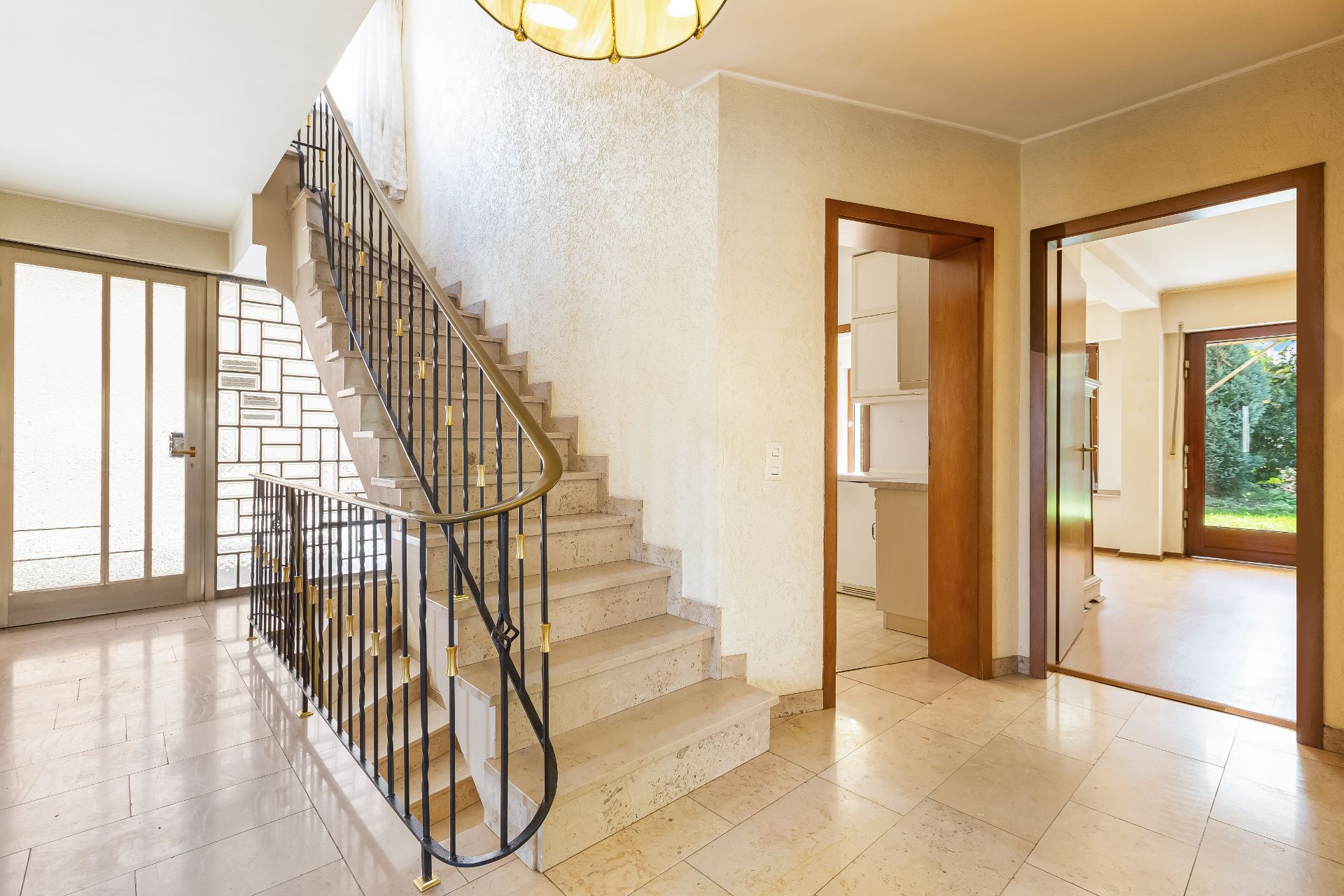 Heller Hausflur mit Steintreppe, Geländer, Türen zu weiteren Räumen und Blick in den Garten.