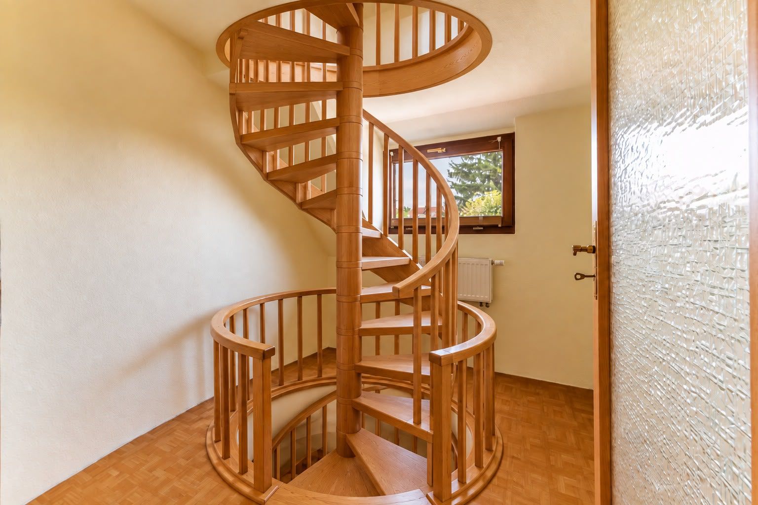 Holz-Wendeltreppe in einem hellen Raum mit Fenster und Parkettboden.