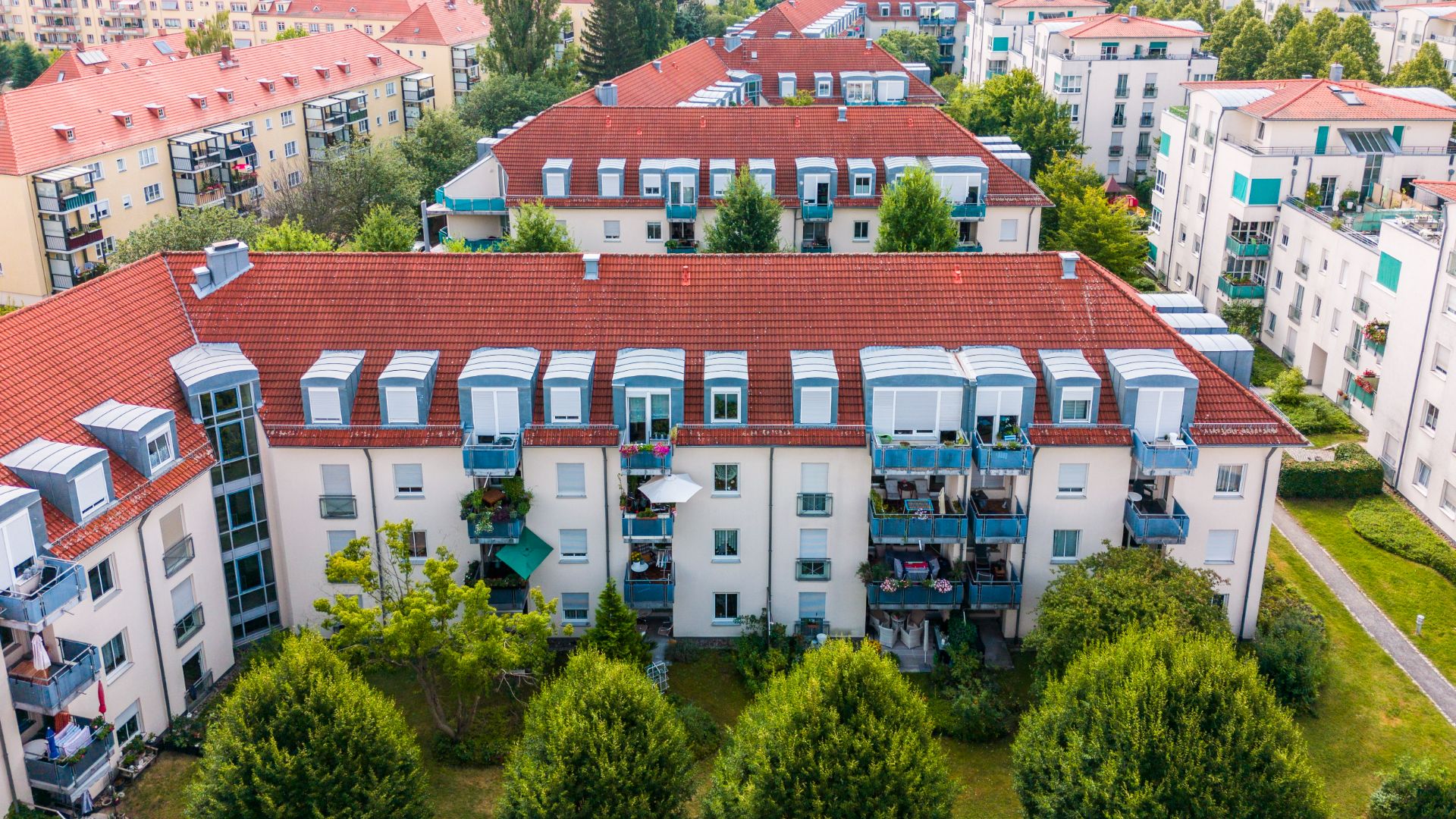 Mehrfamilienhaus mit roten Dächern, Balkonen und Bäumen im Vordergrund.