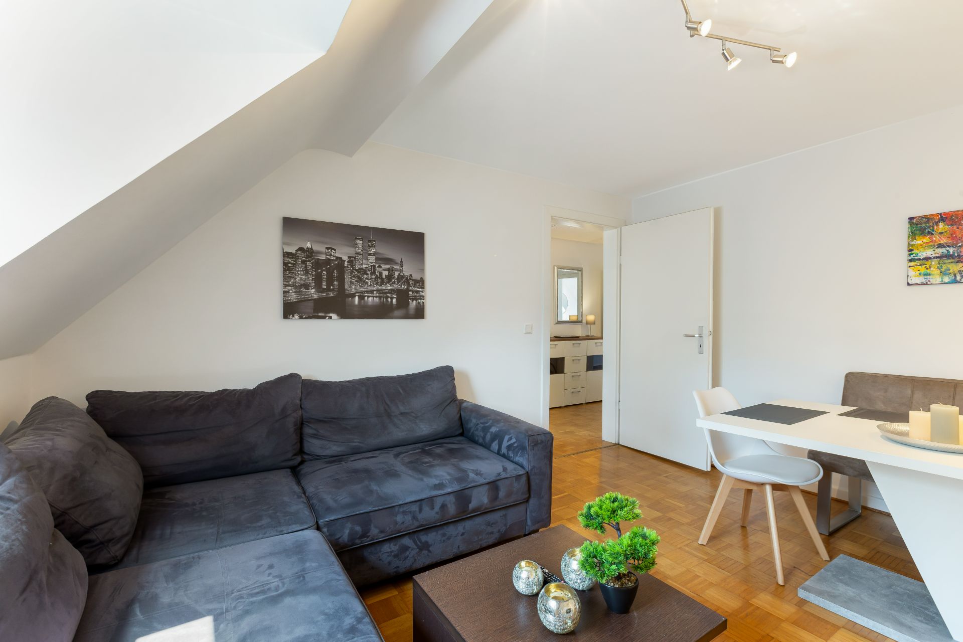 Wohnzimmer mit dunklem Ecksofa, Couchtisch, Esstisch und Wandbildern.