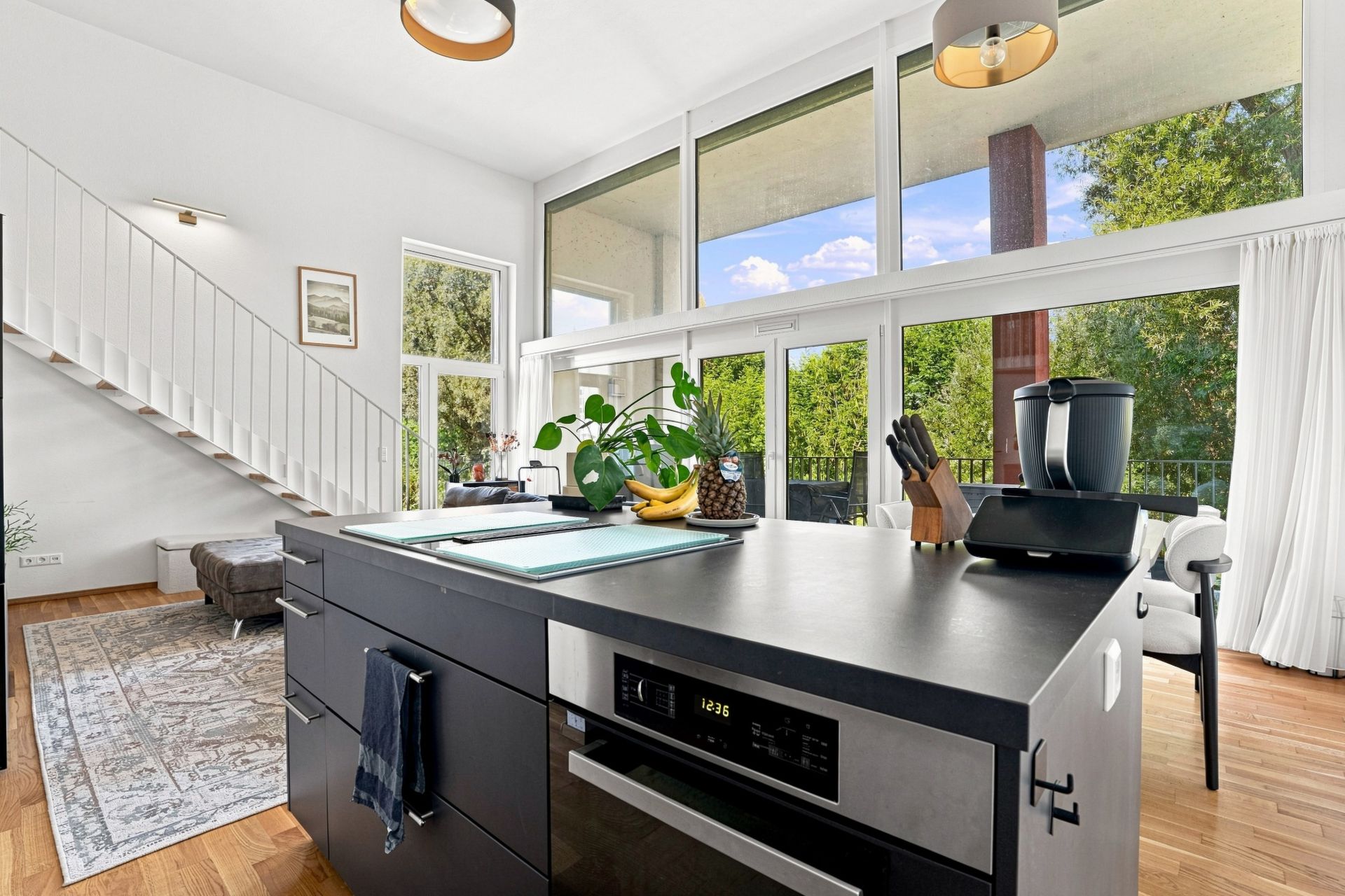 Moderne Küche mit Kücheninsel, großen Fenstern und Blick ins Grüne.