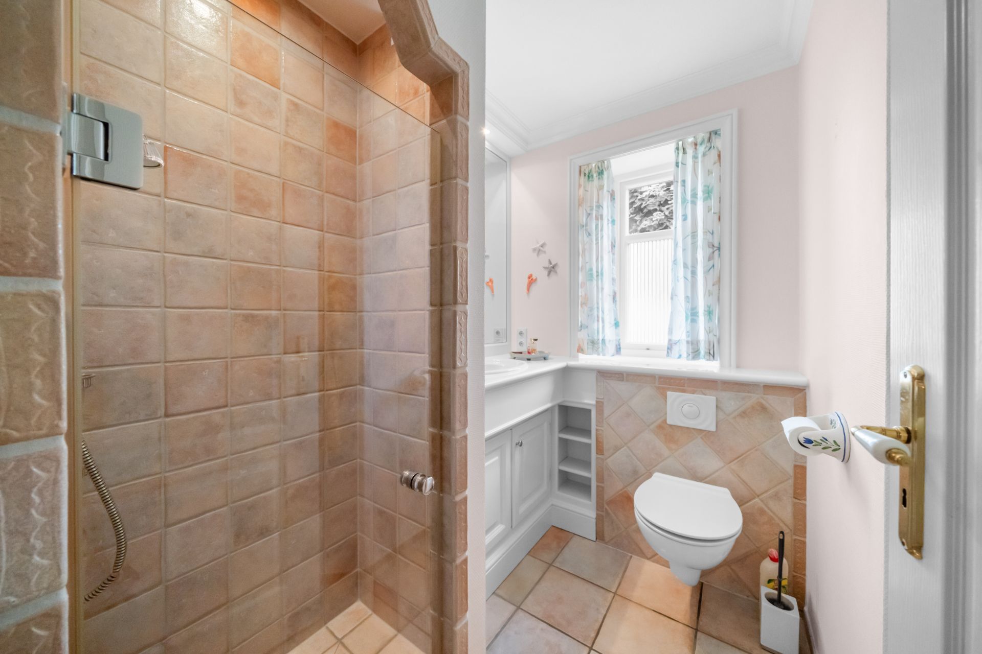 Badezimmer mit begehbarer Dusche, WC und Fenster mit Vorhängen.
