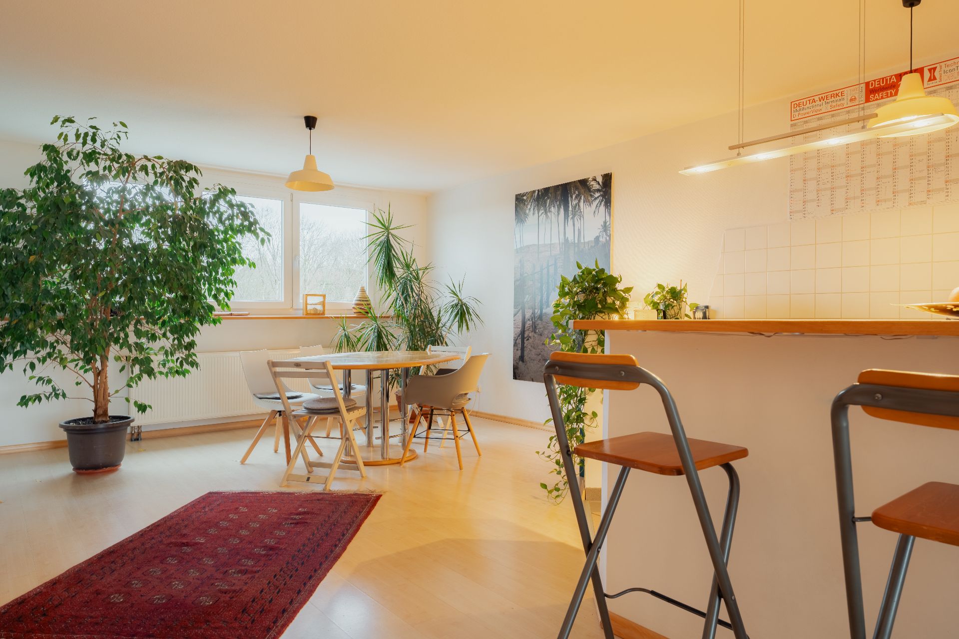 Helles Esszimmer mit Holztisch, Stühlen, Pflanzen, Bartresen und zwei Barhockern.