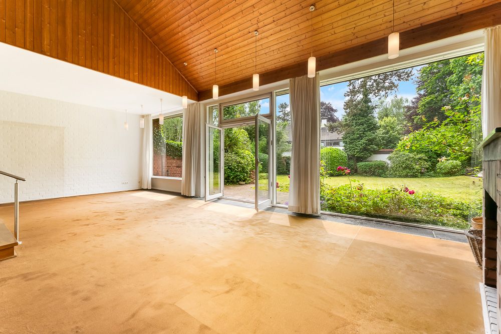 Großes, helles Wohnzimmer mit Teppichboden, Holzdecke und bodentiefen Fenstern zum Garten.