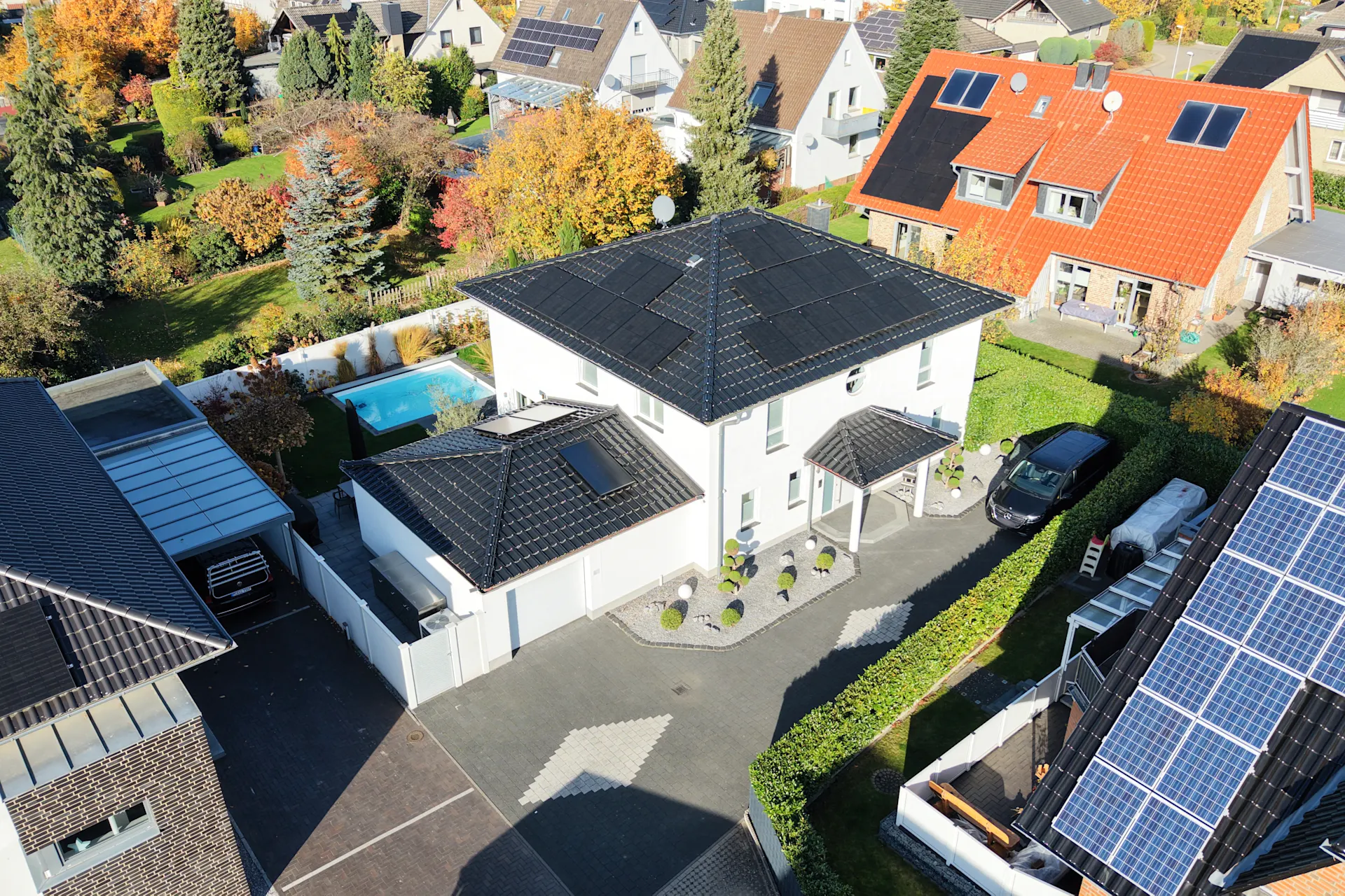 Luftaufnahme eines modernen weißen Einfamilienhauses mit schwarzem Dach und Garten.