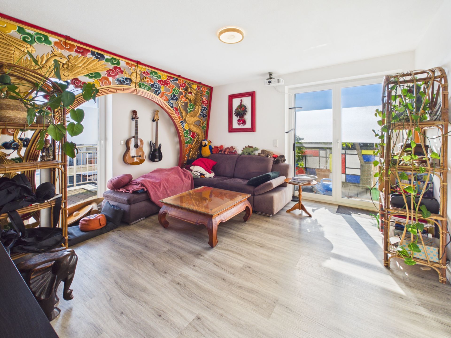 Helles Wohnzimmer mit Sofa, Couchtisch, dekorativem Bogen, Gitarren und vielen Pflanzen.