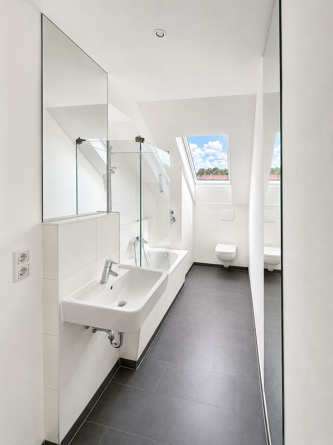 Modernes Badezimmer mit Waschbecken, Badewanne, Toilette und großem Fenster im Dachgeschoss.