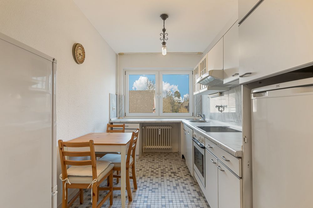 Helle Küche mit Esstisch, vier Stühlen, weißen Schränken und großem Fenster.