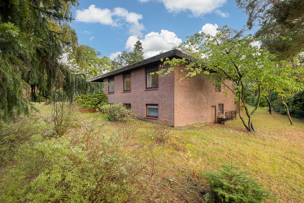 Backsteinwohnhaus mit mehreren Fenstern, umgeben von Bäumen und Garten.