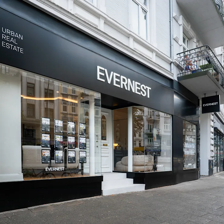Moderne Immobilienagentur mit großer Glasfront und Auslagen an einer Straßenecke.