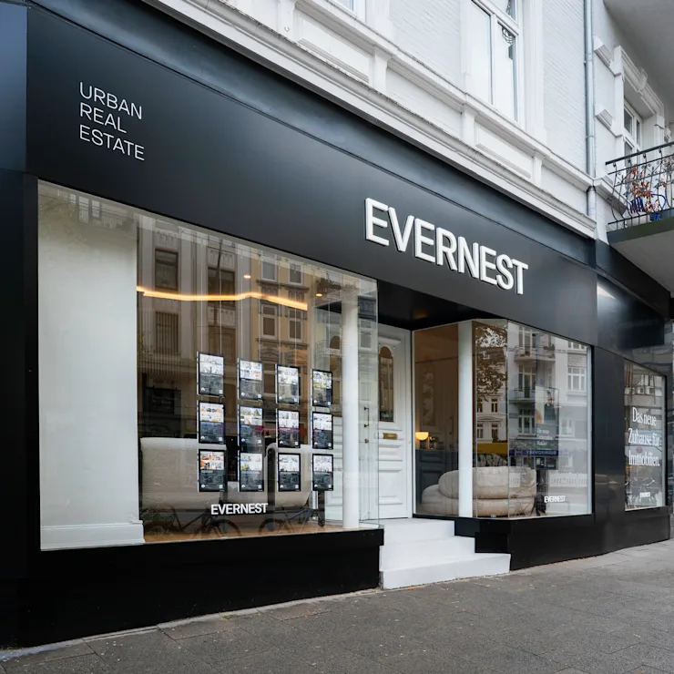 Moderne Immobilienagentur mit großer Glasfront und Auslagen an einer Straßenecke.