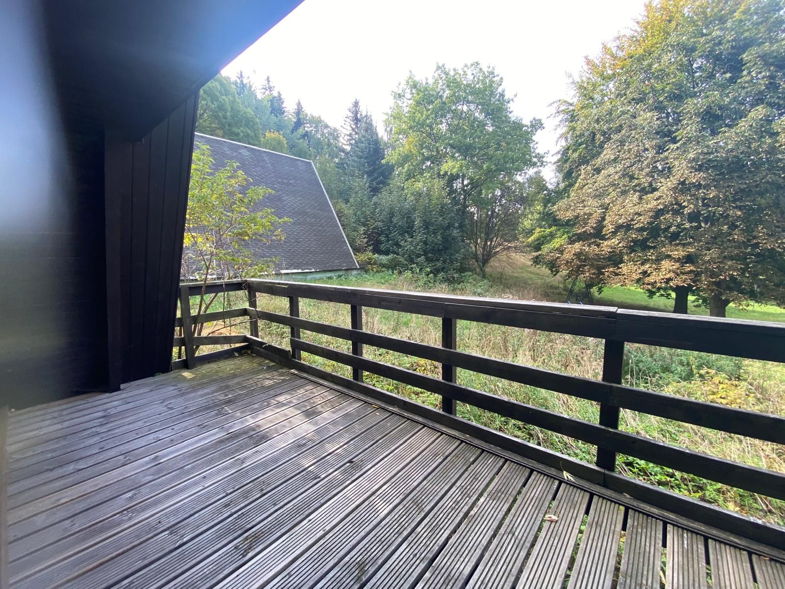 Holzterrasse mit Geländer und Blick auf Bäume und Garten.