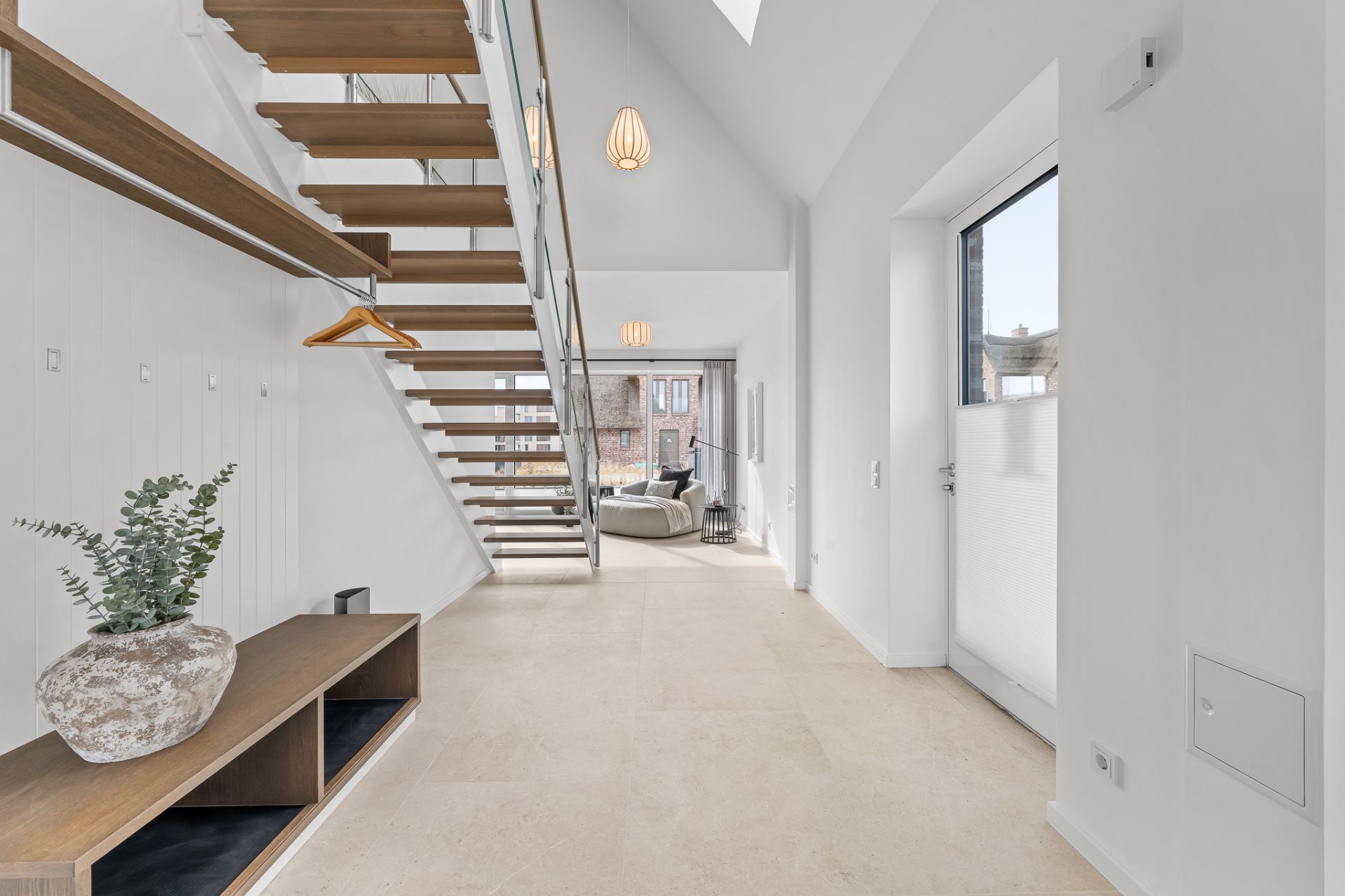 Heller Flur mit offener Holztreppe, Garderobe, Deko-Vase und Blick ins Wohnzimmer.
