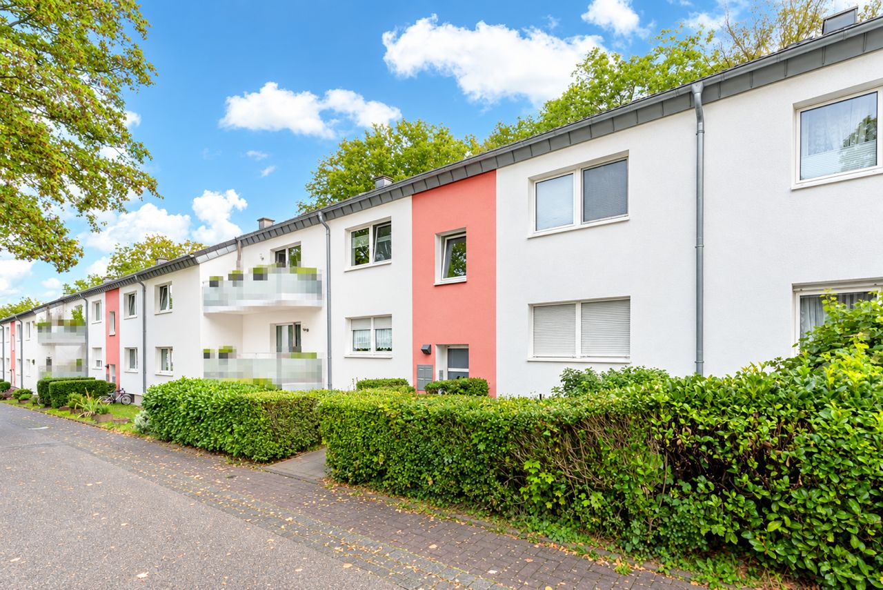 Mehrfamilienhaus mit weißen und roten Fassaden, Balkonen und grünen Hecken an der Straße.