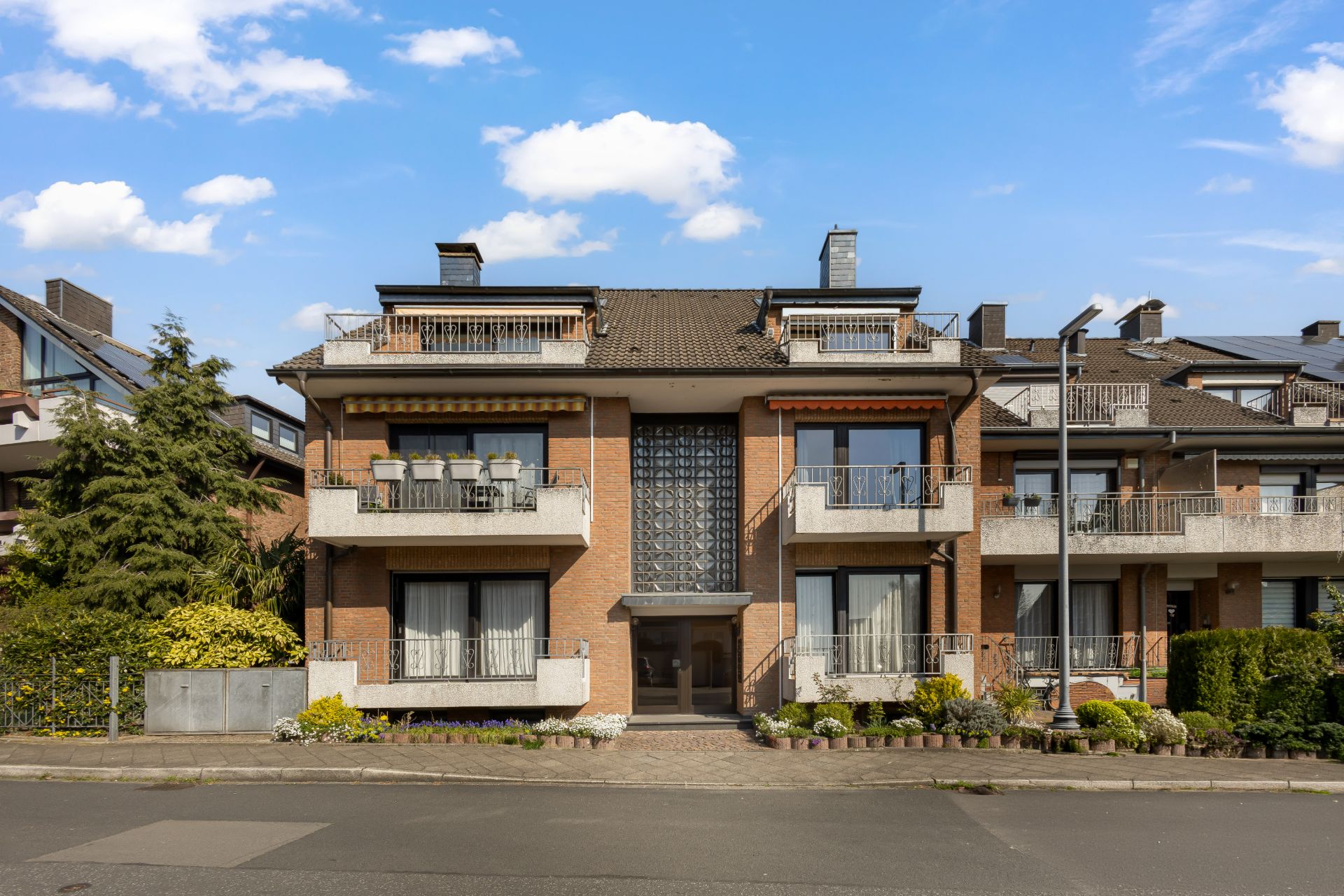 Mehrfamilienhaus mit Balkonen, Vorgarten und zentralem Eingang bei sonnigem Wetter.