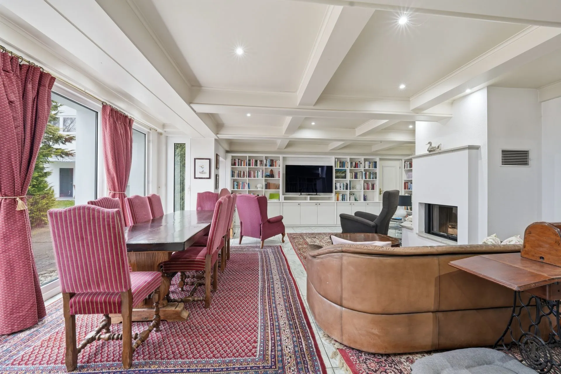 Großes Wohnzimmer mit Esstisch, roten Stühlen, Sofa, Bücherregal und Kamin.