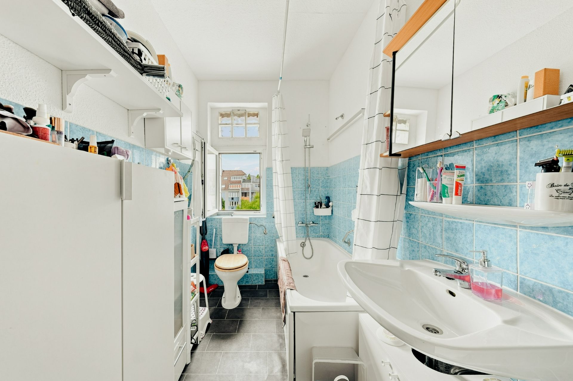 Helles Badezimmer mit Badewanne, Waschbecken, Toilette, blau gefliesten Wänden und großem Fenster.