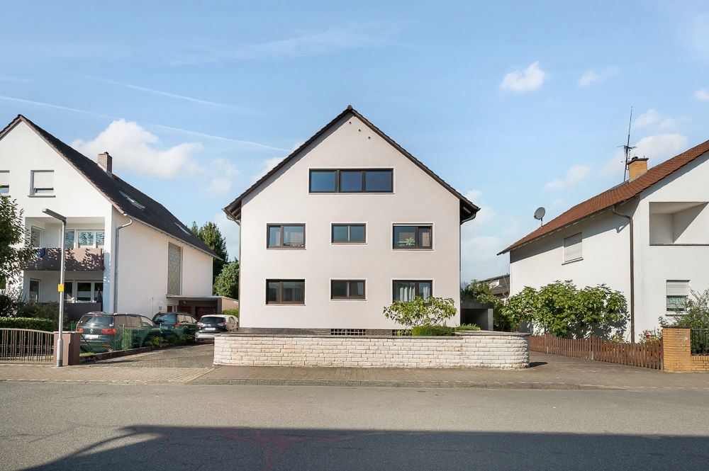 Dreistöckiges Wohnhaus mit Satteldach, weißer Fassade und mehreren Fenstern, umgeben von Nachbarhäusern.