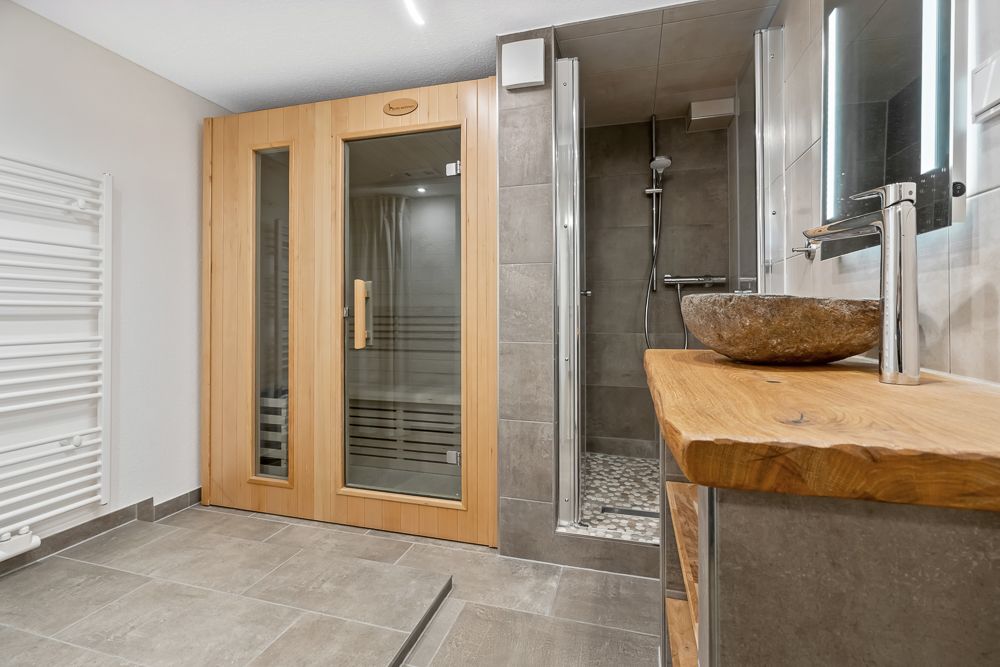 Modernes Badezimmer mit Sauna, Dusche, Waschbecken aus Stein und Holzwaschtisch.