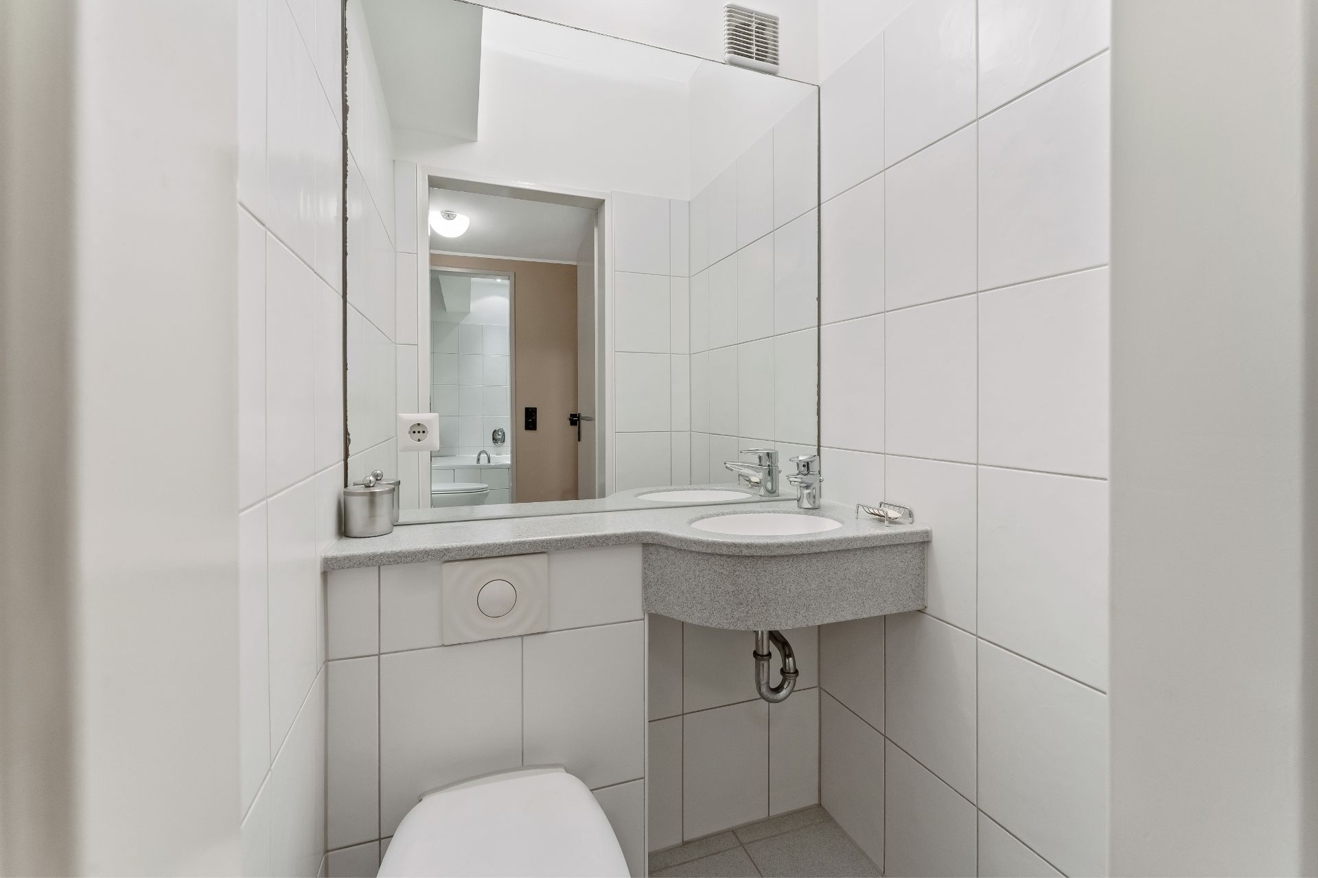 Modernes, weiß gefliestes Badezimmer mit Spiegel, Waschbecken und Toilette.