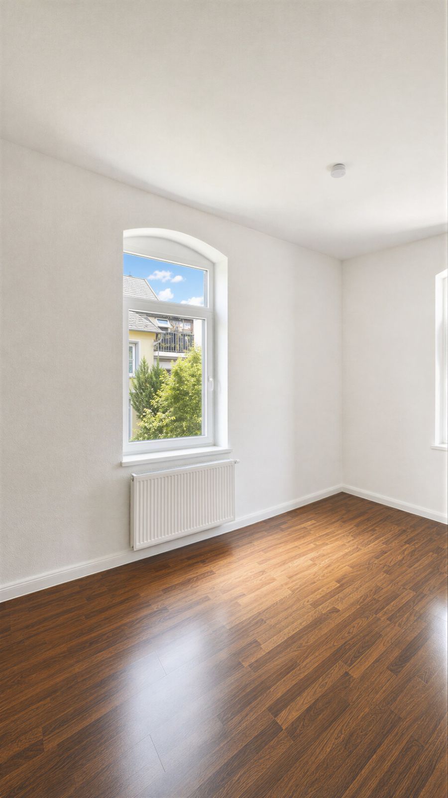 Heller Raum mit Holzboden, weißen Wänden und einem Fenster mit Blick nach draußen.