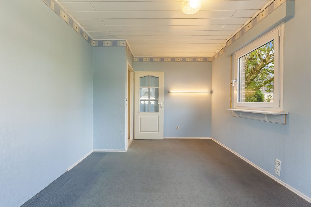 Leeres Zimmer mit hellblauen Wänden, Teppichboden, Fenster und Glastür.