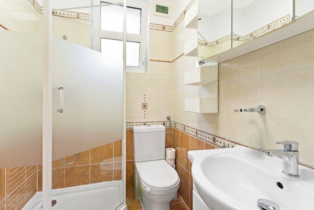 Kleines Badezimmer mit Dusche, Toilette, Waschbecken und Fliesen an den Wänden.
