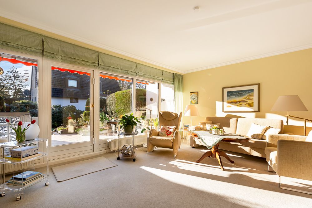Helles Wohnzimmer mit großen Fenstern, Sofa, Sesseln, Couchtisch und Blick auf den Garten.