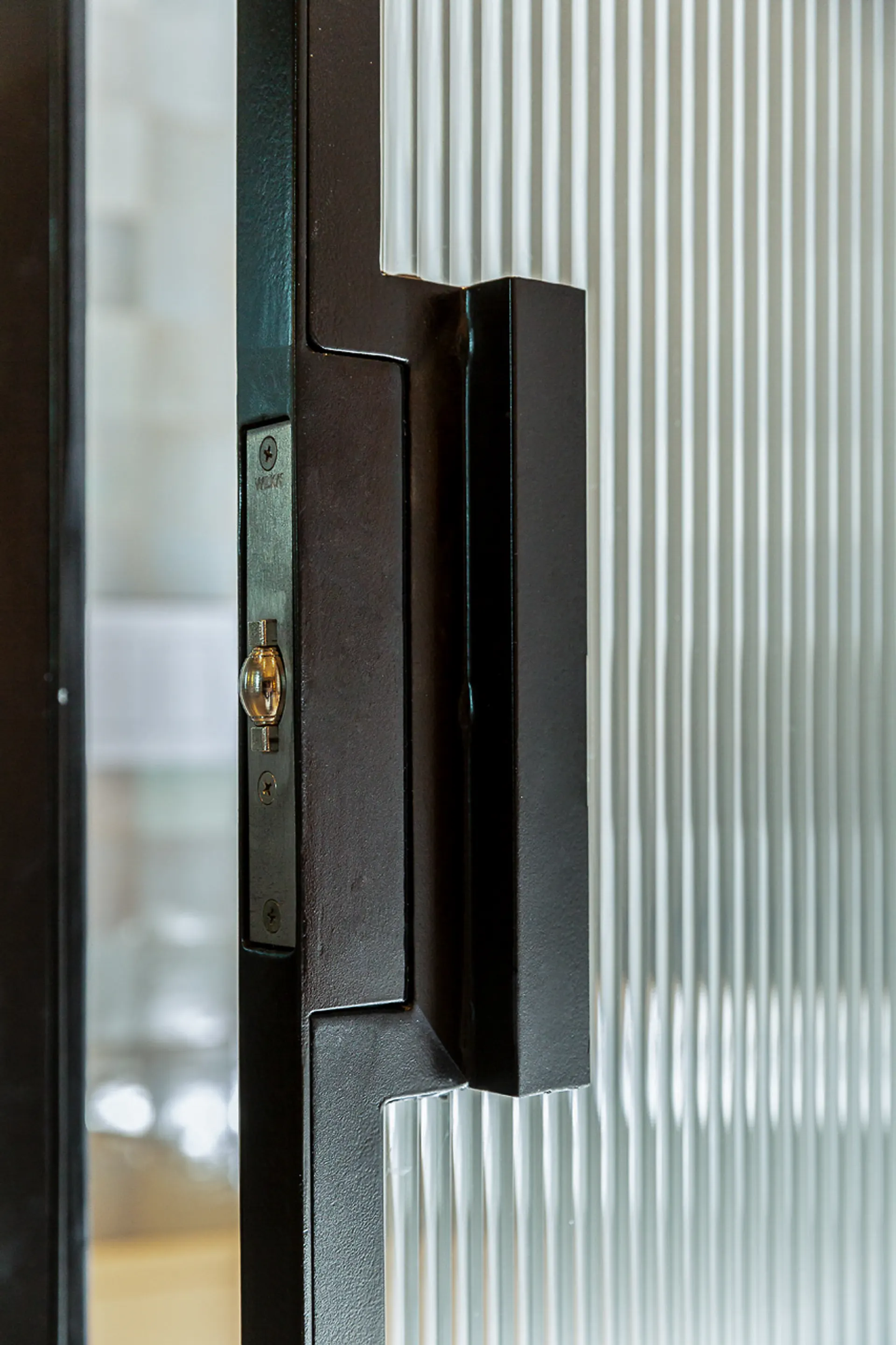 Teilweise geöffnete Glastür mit schwarzem Rahmen und vertikal geriffeltem Glas.
