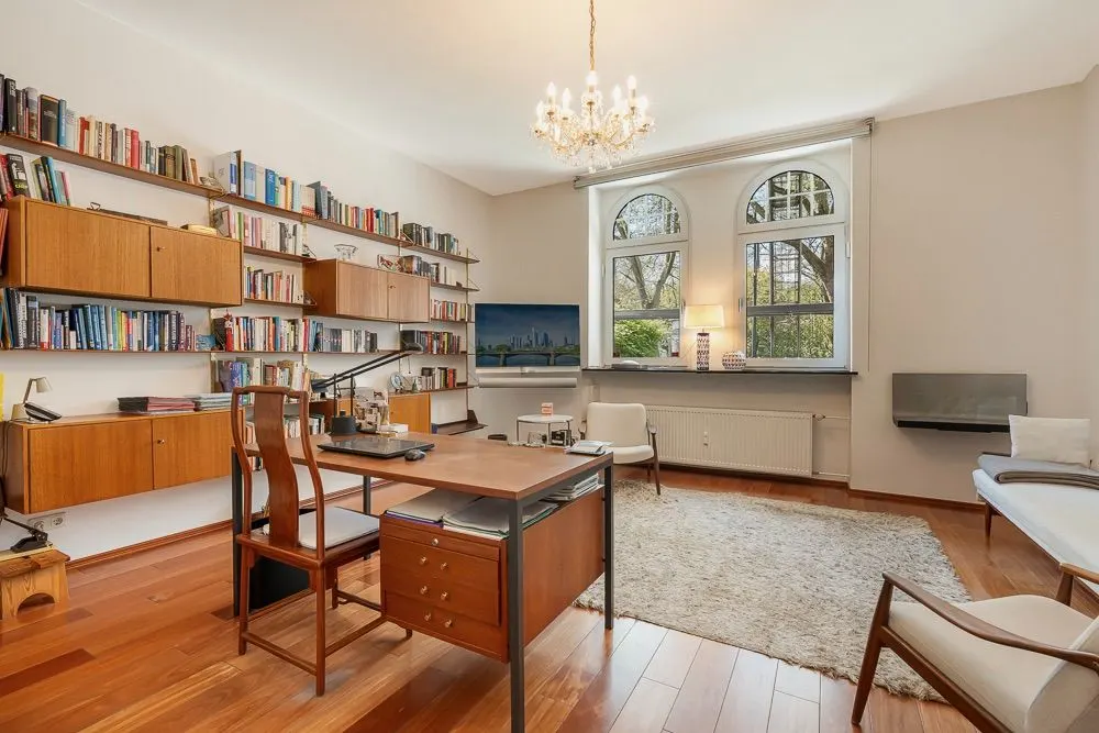 Modernes Arbeitszimmer mit Holzboden, Schreibtisch, Regalen mit Büchern und großen Fenstern.